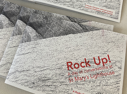 A pile of riso-graph printed pamplets that says 'Rock Up! A day of conversations at St Mary's Lighthouse in red text on a grey grainy background