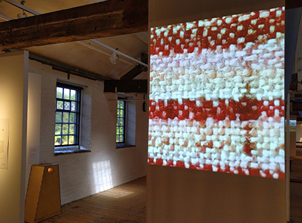 Projected image of a red and white woven textile, onto a textile screen in an old mill building