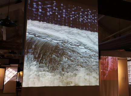 Projected image of a blue and white woven textile combined with a weir, onto a textile screen in an old mill building